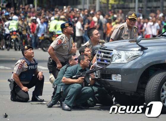 인도네시아 수도 자카르타의 도심 쇼핑몰 인근에서 14일 수차례 폭발이 발생해 최소 3명이 숨진 가운데 현지 경찰이 차량 뒤에 숨어서 상황을 지켜보고 있다.  © AFP=뉴스1 © News1 최종일 기자