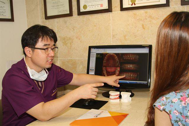 김상운 치과의사가 치아교정을 위해 내원한 환자에게 치아교정 전 후 사진을 보여주고 있다. (사진제공=대구 더블유치과)