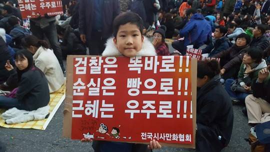 12일 광화문 촛불집회에 참석한 한 아이가 전국시사만화협회가 제작한 피켓을 들고 있다. 사진=전국시사만화협회 제공