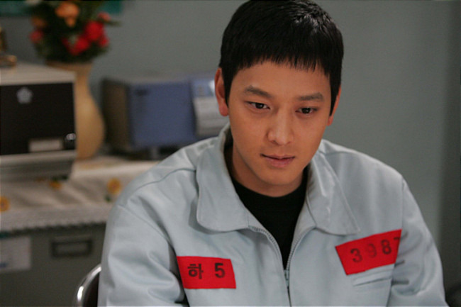 극중 사형수로 나와 빨간 명찰을 착용한 강동원 [사진=우리들의행복한시간]