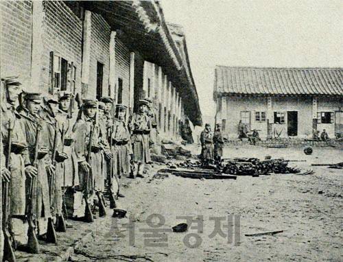 대한제국군 해산 직후 훈련원 모습. 일본군들이 막사 벽에 기대 비를 피하는 가운데 연병장 군데 군데에 대한제국군의 군모와 장비가 보인다.