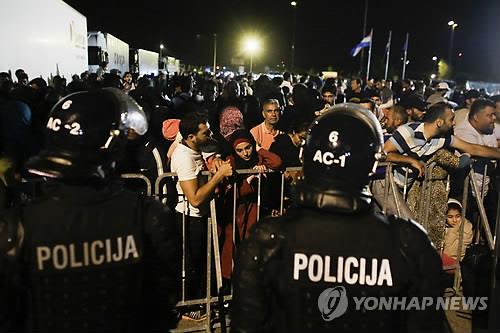 (오브레체<슬로베니아> AP=연합뉴스) 19일 새벽(현지시간) 크로아티아에서 슬로베니아로 넘어가려는 난민들이 슬로베니아 오브레체 검문소에서 가로막혀 펜스 뒤에 서 있다.  난민 수 천 명이 유럽 국가들의 국경 봉쇄, 교량 통행 차단, 철조망 설치 등 난민유입 금지 조치 때문에 곳곳에서 발이 묶였다.