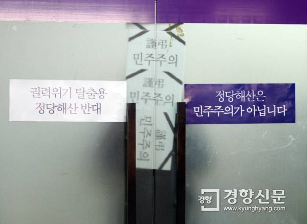헌법재판소가 통합진보당 해산 결정을 내린 2014년 12월19일 서울 대방동 통합진보당 당사에서 한 당직자가 취재진의 촬영을 막기 위해 ‘근조 민주주의’가 적힌 종이를 문틈에 이어붙이고 있다. | 강윤중 기자