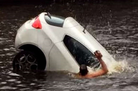 강으로 추락한 차량속 탑승자를 구하기 위해 뛰어든 시민이 큰 돌멩이로 보이는 물건으로 차 유리창을 내리치고 있다. 유튜브 영상 캡처