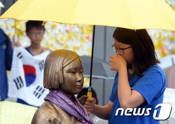 비가 내린  지난6월 5일 오후 서울 종로구 구 일본대사관앞에서 열린 '일본군 위안부 문제 해결을 위한 제 1235차 정기 수요집회'에서 한 학생이 소녀상에 우산을 씌워주고 있다. © News1 최현규 기자