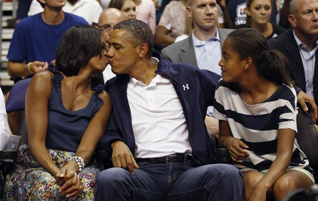 미국 퍼스트레이디 미셸 오바마(왼쪽)가 남편인 버락 오바마 대통령과 2012년 농구 경기를 관람하던 중 키스타임에 걸려 입을 맞추고 있다. 오른쪽은 큰 딸 말리아.  연합뉴스