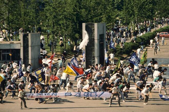 1987년 6월9일 서울 연세대학교 앞에서 이한열 열사가 피격되기 직전의 모습. 왼쪽 흰 현수막 뒤에 영문자로 ‘연세’라고 쓰인 티셔츠를 입고, 파란색 마스크를 쓰고 있는 이한열 열사의 모습이 보인다. 네이선 벤 제공