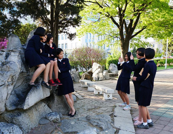 평양 대동문 인근에서 핸드폰 사진을 찍고 있는 북한 여고생들. 턱을 괴고 팔을 마주잡으며 포즈를 취한 친구를 보며 한 여학생이 박장대소하고 있다.[Sejin Pak 페이스북]