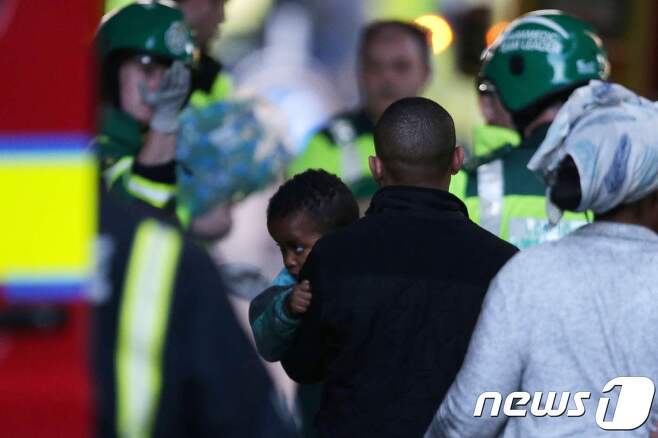 런던 화재 현장에서 꼬마를 옮기고 있는 한 남성과 현지 구조 당국. © AFP=뉴스1