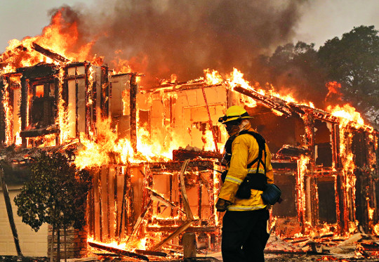 미국 캘리포니아주 소노마카운티의 샌타로자시에서 9일(현지시간) 소방관이 불타는 집을 바라보고 있다. 산불이 강풍을 타고 단숨에 캘리포니아주 북부로 번지면서 1500채의 주택과 상가 등을 태웠다. 소방당국은 불을 진화하기보다 주민 대피에 힘을 쏟고 있다. AP뉴시스