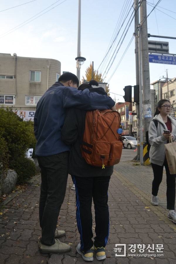 2016학년도 대학수학능력시험이 치러진 2015년 11월 12일 한 학부모가 경기 안산시 원곡고 정문 앞에서 가방에 세월호를 상징하는 노란 리본을 단 수험생의 어깨를 끌어안고 기도하고 있다. 경향신문 자료사진