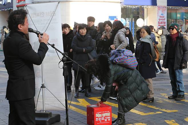 노래를 듣던 한 시민이 모금함에 돈을 넣고 있다. 신인섭 기자