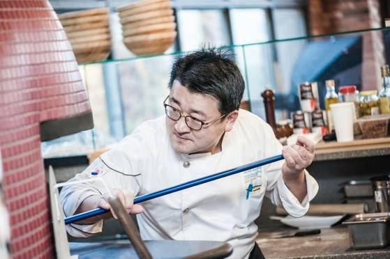 청와대 근무할 때의 조리복을 입은 한상훈 셰프가 구울 피자를 화덕에 밀어 넣고있다.