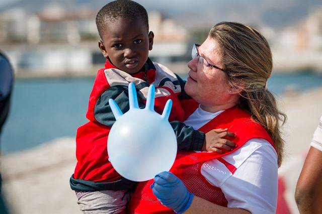 스페인  모트릴항에 26일(현지시간)  지중해에서 구조된 난민들 도착한 가운데 한 난민 어린이가 장갑으로 만든 풍선을 든 스페인 적십자 요원의 품에 안겨 있다. 로이터 연합뉴스