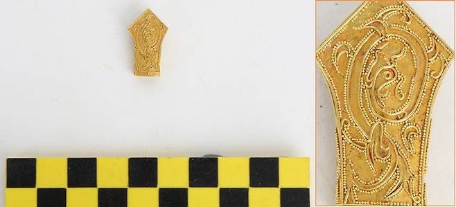 2호 무덤에서 나온 용무늬 금속장식. 위쪽 끝이 뾰족한 오각형의 모양새를 하고 있다. 표면에 미세한 금속알갱이를 이어붙인 정교한 기법으로 몸 틀며 비상하는 용의 무늬를 넣어 눈길을 끈다.