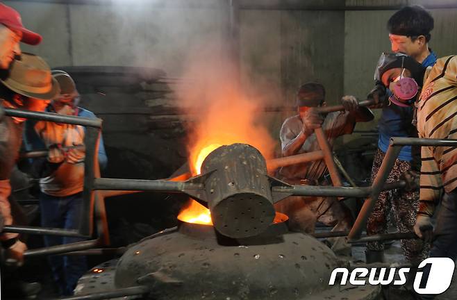 29일 경북 구미시 고아읍 사랑채 가마솥공장에서 직원들이 살이 타들어가는 무더위와 싸우며 지름 1m 크기의 대형 무쇠 가마솥 거푸집에 1500도에서 선철을 녹여 만든 쇳물을 붓고 있다.2018.7.29/뉴스1 © News1 정우용 기자