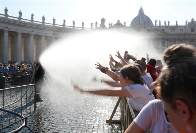 바티칸 성 베드로 광장에서 31일(현지시간) 프란치스코 교황의 도착을 기다리던 사람들이 소방관이 뿌려주는 물을 맞으며 더위를 식히고 있다. 로이터 연합뉴스