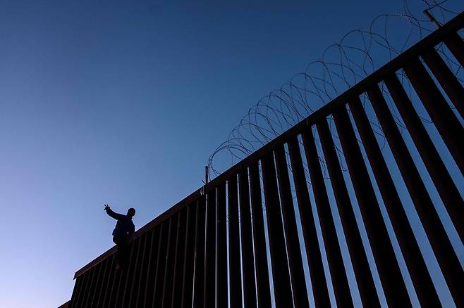 한 이민자가 18일(현지시간) 멕시코 티후아나 미국-멕시코 국경 담장 위에 서 있다. [AFP=연합뉴스]