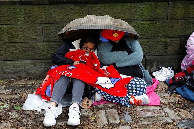 방탄소년단 팬들이 14일(현지시간) 뉴욕 센트럴 파크에서 우산을 쓰고 잠을 청하고 있다. [로이터=연합뉴스]