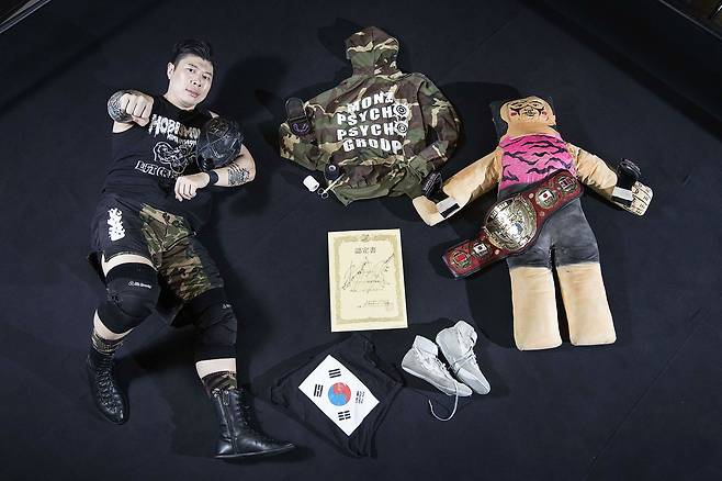 프로레슬러 김남석선수가 유니폼, 챔피언 벨트, 챔피언 인증서 등과 함께 링 위에 누웠다. 오른쪽은 인형 프로레슬러 '뉴릴디'. 피트의 마스코트로 실제 링 위에서 선수들과 경기를 하기도 한다. 장진영 기자