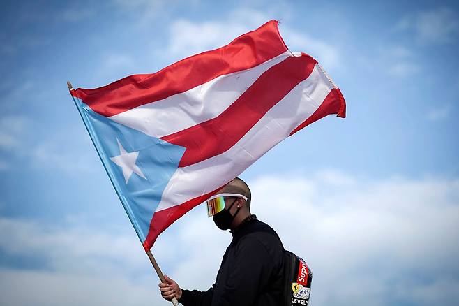 17일(현지시간) 푸에르토리코 수도인 산후안에서 열린 리카르도 로세요 주지사 해임 요구 시위에서 미국 래퍼 배드 버니가 국기를 들고 있다. 배드 버니는 산후안 출생이다. [AFP=연합뉴스]