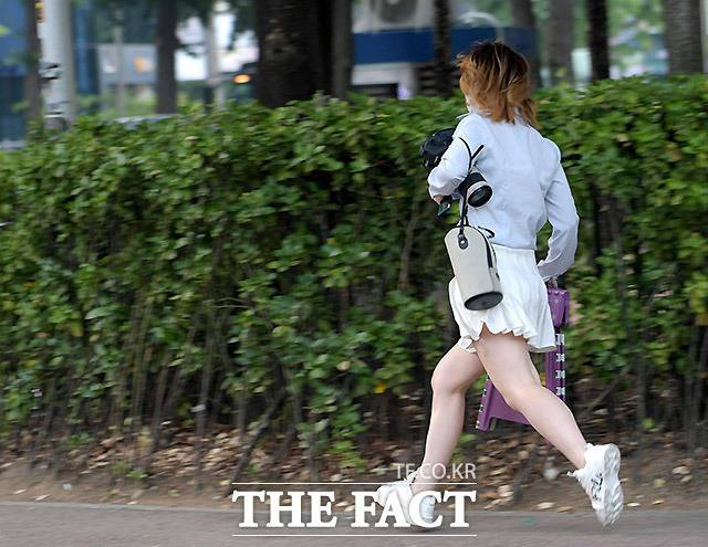 현장에 늦은 한 여성이 하이엔드급 DSLR 보디와 의자를 들고 뛰어가고 있다.