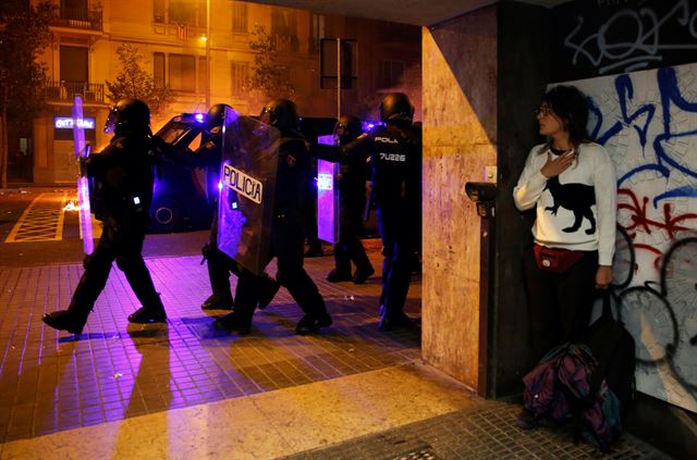 스페인 대법원이 카탈루냐주의 분리독립 지도부에 대해 최대 13년의 중형을 선고함에 따른 항의 시위 사흘째 계속 되고 있는 가운데 16일(현지시간) 바르셀로나에서 한 여성이 몸을 숨긴 채  진압경찰들이 지나가는 모습을 바라보고 있다.  로이터 연합뉴스