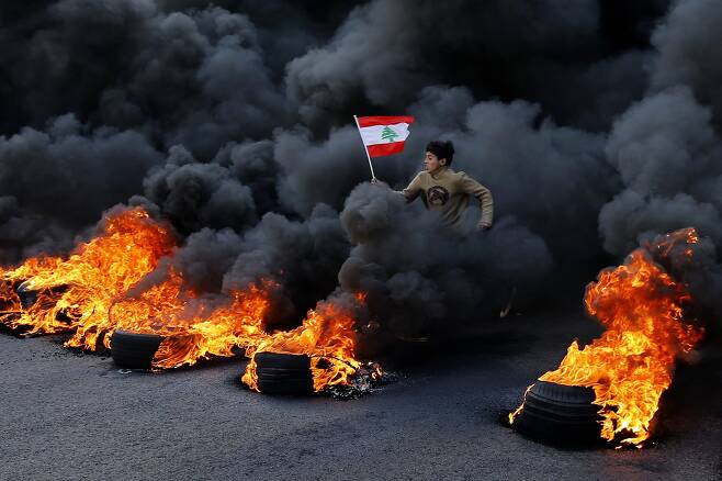 14일(현지시간) 레바논 수도 베이루트 북쪽 잘엘딥 시내에서 한 시위자가 주요도로 봉쇄를 위해 불을 질렀던 타이어 위로 뛰어나오고 있다.[EPA=연합뉴스]