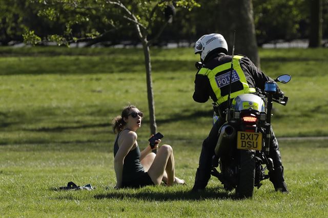 5일 영국 런던의 프림로즈 힐 공원에서 한 순찰 경관이 일광욕을 즐기는 한 여성에게 집으로 돌아갈 것을 권유하고 있다. 런던=AP 연합뉴스