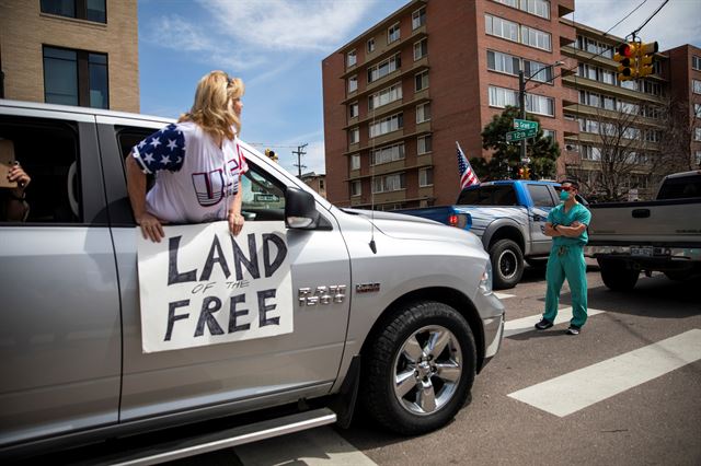미국 콜로라도주 덴버에서 19일 코로나19 확산 방지를 위한 자택대피령에 반대하는 시위가 열리고 있는 가운데 의료진들이 차량시위자들을 막고 서 있다. 콜로라도=로이터 연합뉴스