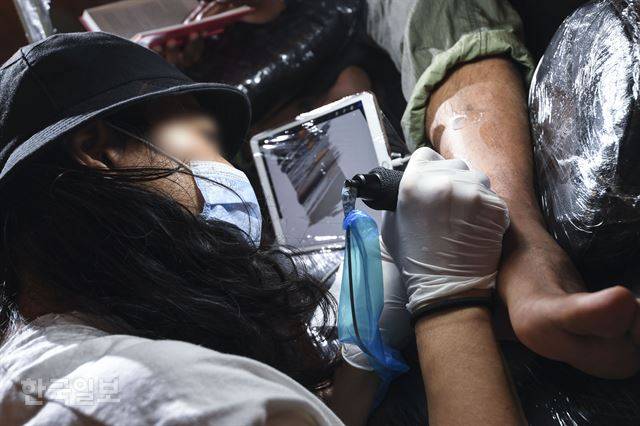 타투이스트 백모씨가 지난 22일 오후 서울 마포구 성산동 작업실에서 고객 발목에 문신을 새겨 넣고 있다. 백씨는 일회용 바늘이 꽂힌 기계에 잉크를 조금씩 묻혀가며 붓질하듯이 바다 그림을 그렸다. 이한호 기자