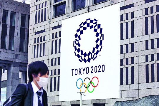 일본 도쿄의 한 시민이 지난 3월 23일 시내 건물에 설치된 2020 도쿄올림픽 포스터 현수막 앞을 마스크를 쓴 채로 지나가고 있다. AP연합뉴스
