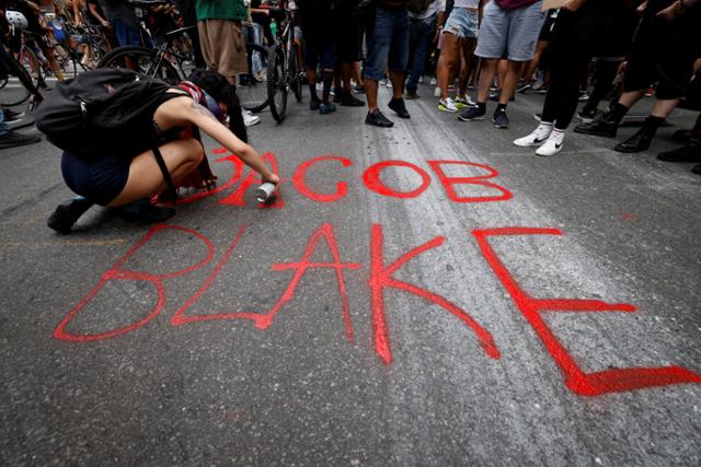 24일 미국 뉴욕 맨해튼에서 인종차별 규탄 시위에 참가한 한 여성이 전날 위스콘신에서 경찰이 쏜 총에 맞아 중태에 빠진 비무장 흑인 남성 '제이컵 블레이크'의 이름을 거리 바닥에 페인트로 적고 있다. 뉴욕=로이터 연합뉴스