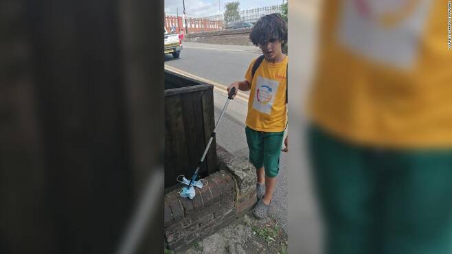 11세 소년 대니 아이소이가 거리에서 집게로 수거한 마스크를 들어 보이고 있다.(사진=샬럿 러베니 제공)