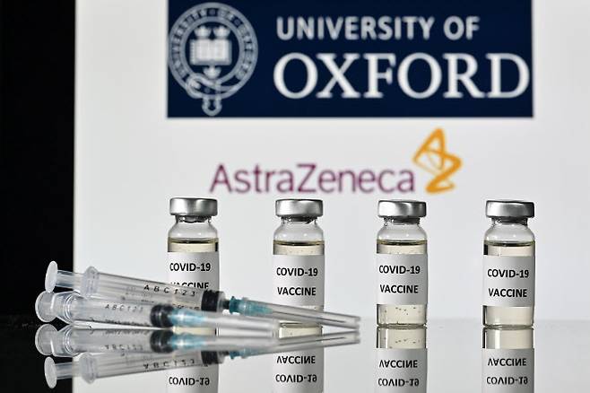 아스트라제네카와 옥스퍼드대학 로고를 배경으로 코로나19 백신 스티커가 부착된 유리병과 주사기가 놓여 있는 모습. (사진=AFP)