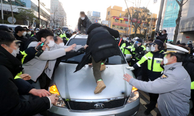 형기를 마치고 출소한 아동 성범죄자 조두순이 탑승한 관용차량이 지난 12일 오전 경기도 안산시 법무부안산준법지원센터에서 나오던 중 일부 시민과 유튜버 등에 가로막혀 있다/연합뉴스