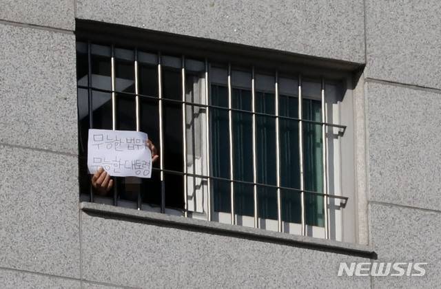 [서울=뉴시스]고범준 기자 = 서울동부구치소에 대한 6차 전수검사에서 수용자 66명이 추가로 신종 코로나바이러스 감염증(코로나19) 확진 판정을 받아 누적 확진자가 현재까지 1,161명으로 집계된 6일 서울 송파구 서울동부구치소에서 한 수용자가 종이에 쓴 글을 취재진에게 보여주고 있다. 내용은 '무능한 법무부 무능한 대통령'이라고 적혀있다. 2021.01.06. bjko@newsis.com