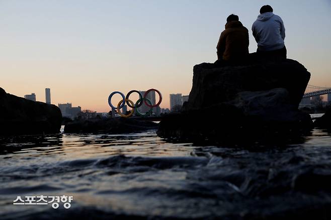 두 남성이 지난 14일 일본 도쿄의 한 바닷가 바위 위에 앉아 오륜기 조형물을 바라보고 있다. 도쿄 | 로이터연합