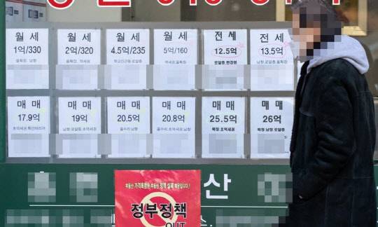 한 시민이 부동산 매물정보와 정부의 부동산 정책을 규탄하는 포스터가 걸린 공인중개업소 앞을 지나가고 있다. <연합뉴스>