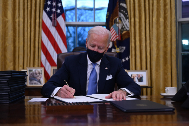 조 바이든 미국 대통령이 20일(현지 시간) 워싱턴DC 백악관 집무실에서 취임 이후 첫 업무로 파리 기후변화협약 복귀, 연방 시설 내 마스크 착용 의무화, 인종 평등 보장 등 행정명령 17건에 서명하고 있다.   /AFP연합뉴스
