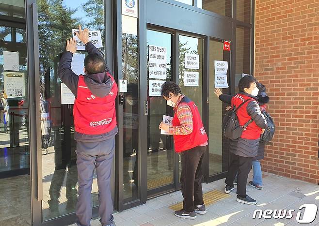신라대학교 청소용역 해고 노동자들이 기자회견 후 대학본부 입구에 '집단해고 철회' 문구를 부착하고 있다.2021.1.27/뉴스1 노경민 기자©