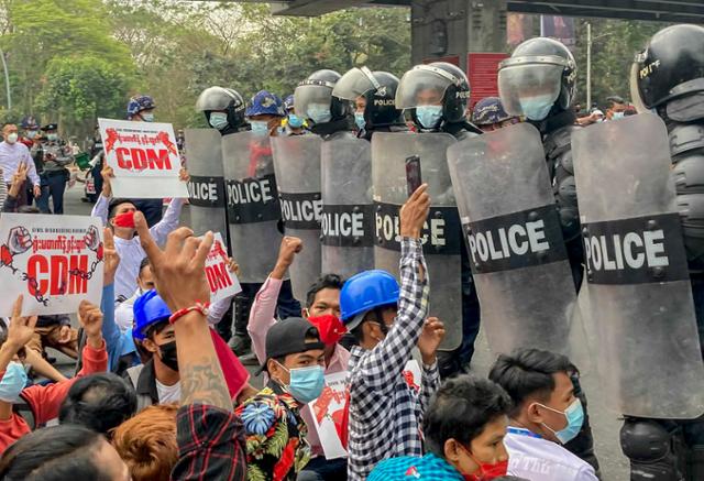 18일(현지시간) 미얀마 최대도시 양곤에서 쿠데타 항의 시위대가 '시민 불복종 운동'(CDM·Civil Disobedience Movement)을 촉구하는 팻말을 들고 '세 손가락 경례'를 하며 진압경찰과 대치하고 있다. 양곤=AP 연합뉴스