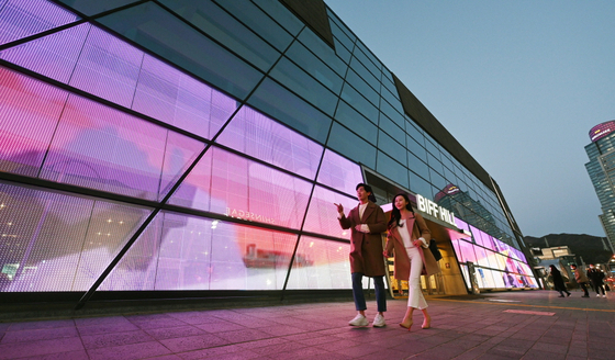 Models walk in front of the Busan Cinema Center in Busan on Wednesday. LG Electronics installed transparent LED film on the glass walls of the center as form of media art. [YONHAP]