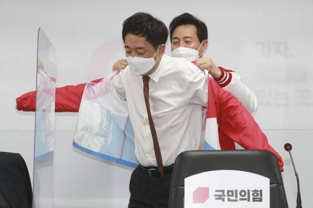국민의힘 오세훈 서울시장 후보가 24일 오전 서울 여의도 중앙당사에서 열린 선거대책위원회 회의에서 금태섭 공동선거대책위원장에게 당 점퍼를 입혀주고 있다. 연합뉴스