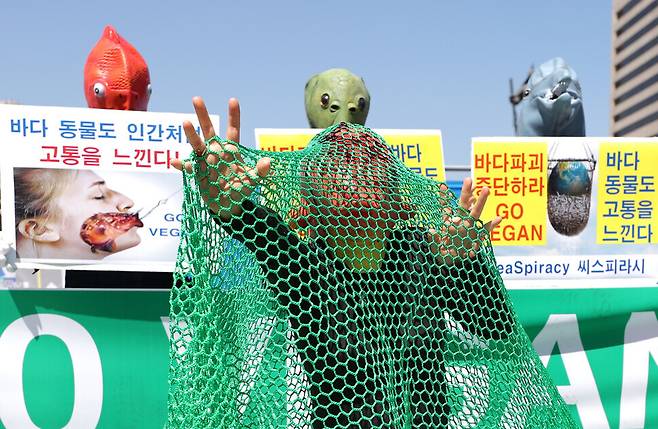 One of the protesters wearing a fish mask pretends to be a fish in a fishing net in a street performance staged after the press conference. (Lee Jong-keun/The Hankyoreh)