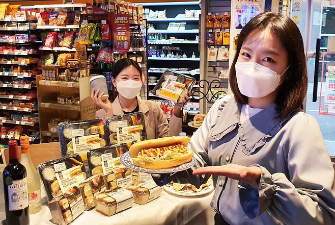 18일 성동구 소재 이마트24 성수대우점에서 모델이 프리미엄 식사 대용 빵 상품인 시그니처 오리지널 핫도그와 베이글 샌드위치 2종을 소개하고 있다.