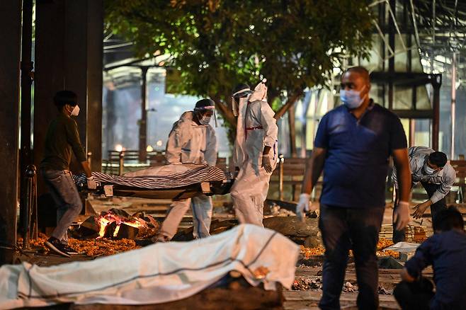 인도 수도 뉴델리의 야무나 강둑에 마련된 화장터에서 22일(현지 시각) 새벽 직원들이 코로나 사망자들의 시신을 옮기고 있다. /AFP 연합뉴스