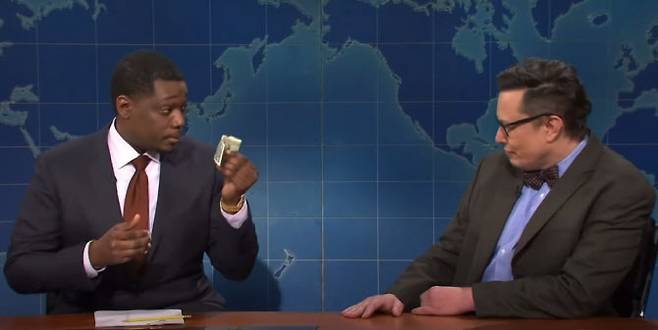 SNL 위켄드 업데이트에서 마이클 체(왼쪽)가 일론 머스크(오른쪽)에게 1달러 지폐를 꺼내 보이며 “이게 진짜”라고 말하고 있다(사진=SNL)