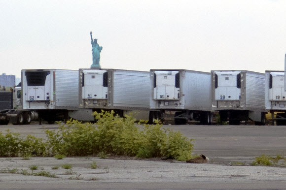 지난 6일(현지시간) 미국 뉴욕 자유의 여신상이 보이는 곳에 코로나19로 사망한 이들은 보관한 냉장트럭들이 줄지어 서 있는 모습. AP
