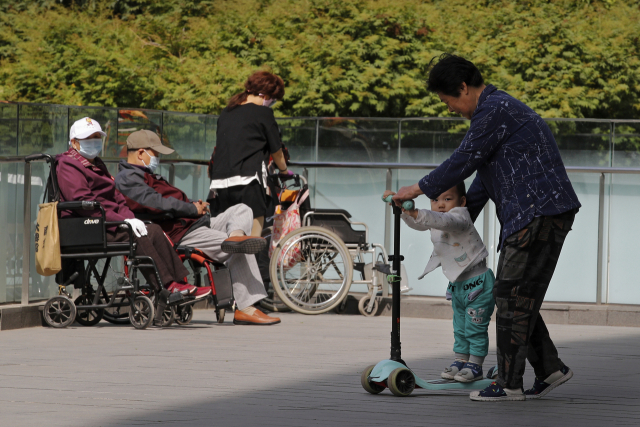 지난 10일 중국 베이징의 한 공원에서 할머니가 손주를 돌보고 있다. 휠체어에 앉은 노인들의 모습에 중국의 저출산·고령화 문제가 묻어난다. /AP연합뉴스